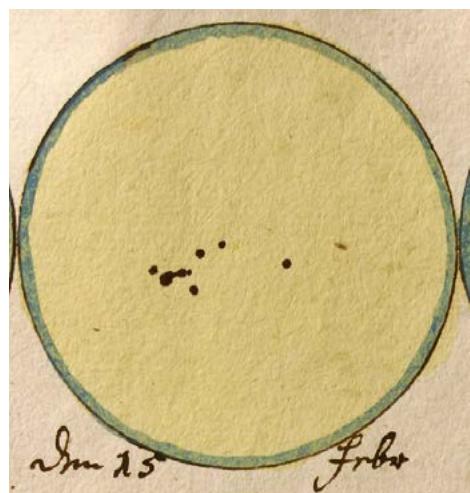 Figure 3.5: The image displays a hand-drawn illustration of the Sun, showing a circular solar disk with a pale yellow surface and a thin blue-green outer ring, consistent with 18th-century astronomical drawings. Several dark, irregularly shaped spots are visible on the solar surface, clustered in two groups, representing sunspots observed on February 15, 1760. Handwritten annotations below the disk include 'd (source: reference 62)
